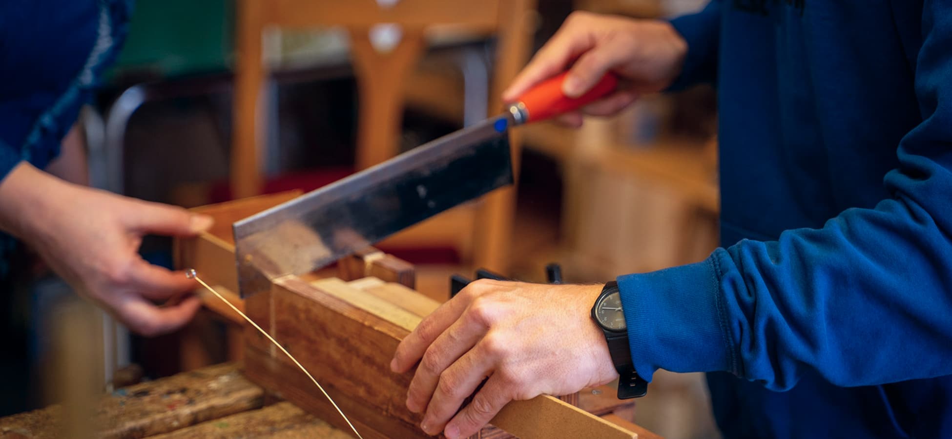 Zwei Personen sägen gemeinsam ein Holzbrett in einer handwerklichen Werkstatt